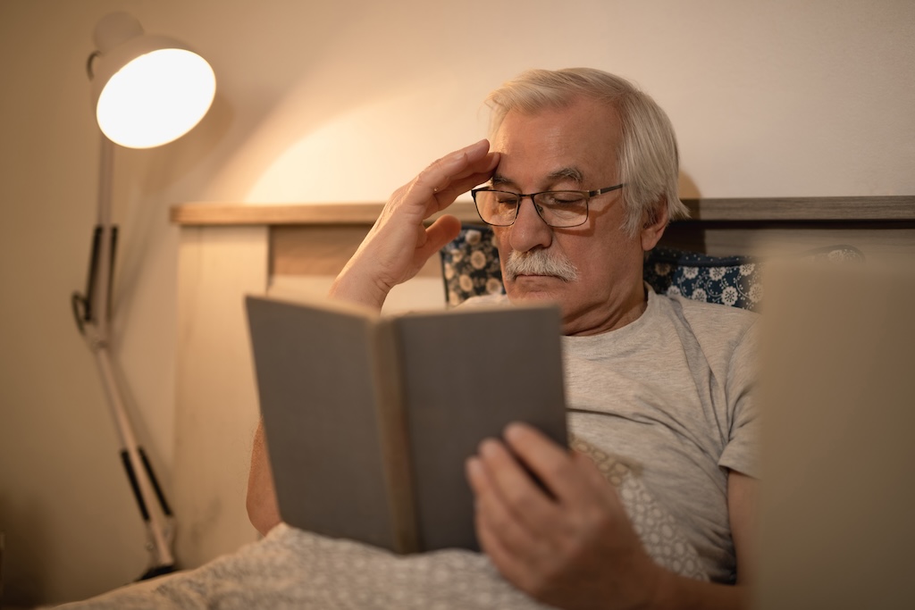 Senior man reading a book while lying down in bed